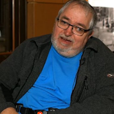 GDA Trustee, Alan Dick - Alan has short grey hair and a short grey beard, and is wearing glasses, a grey fleece and bright blue t-shirt.