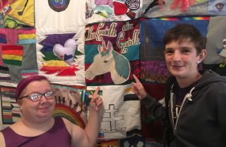 Two GDA members smile and point to a colourful collage of rainbow images on the wall behind them including a unicorn