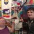 Two GDA members smile and point to a colourful collage of rainbow images on the wall behind them including a unicorn