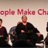 GDA's Purple Poncho Players on stage in a row, singing and looking defiantly ahead - in the background large pink letters read 'People Make Change'