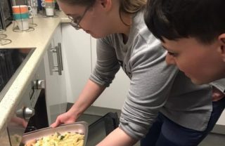 With support, a visually impaired member puts a meal they have made in an oven.