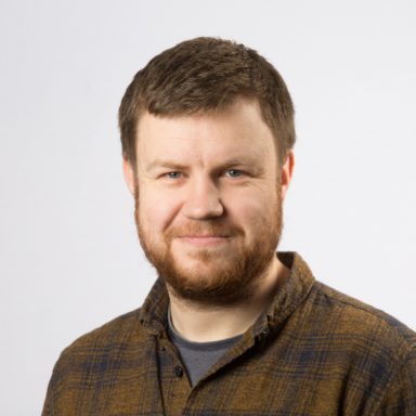 Headshot of Ian MacCorquodale who has dark hair, and a beard.