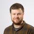 Headshot of Ian MacCorquodale who has dark hair, and a beard.