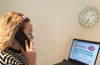 Wellbeing adviser on the phone, looking at GDA's website on a computer on a stand.