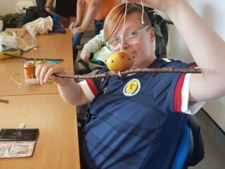 Young disabled person holds up a bird feeder that they've made from things they found outdoors.