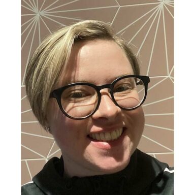 Stephanie smiles at the camera, with short blonde hair and dark glasses.